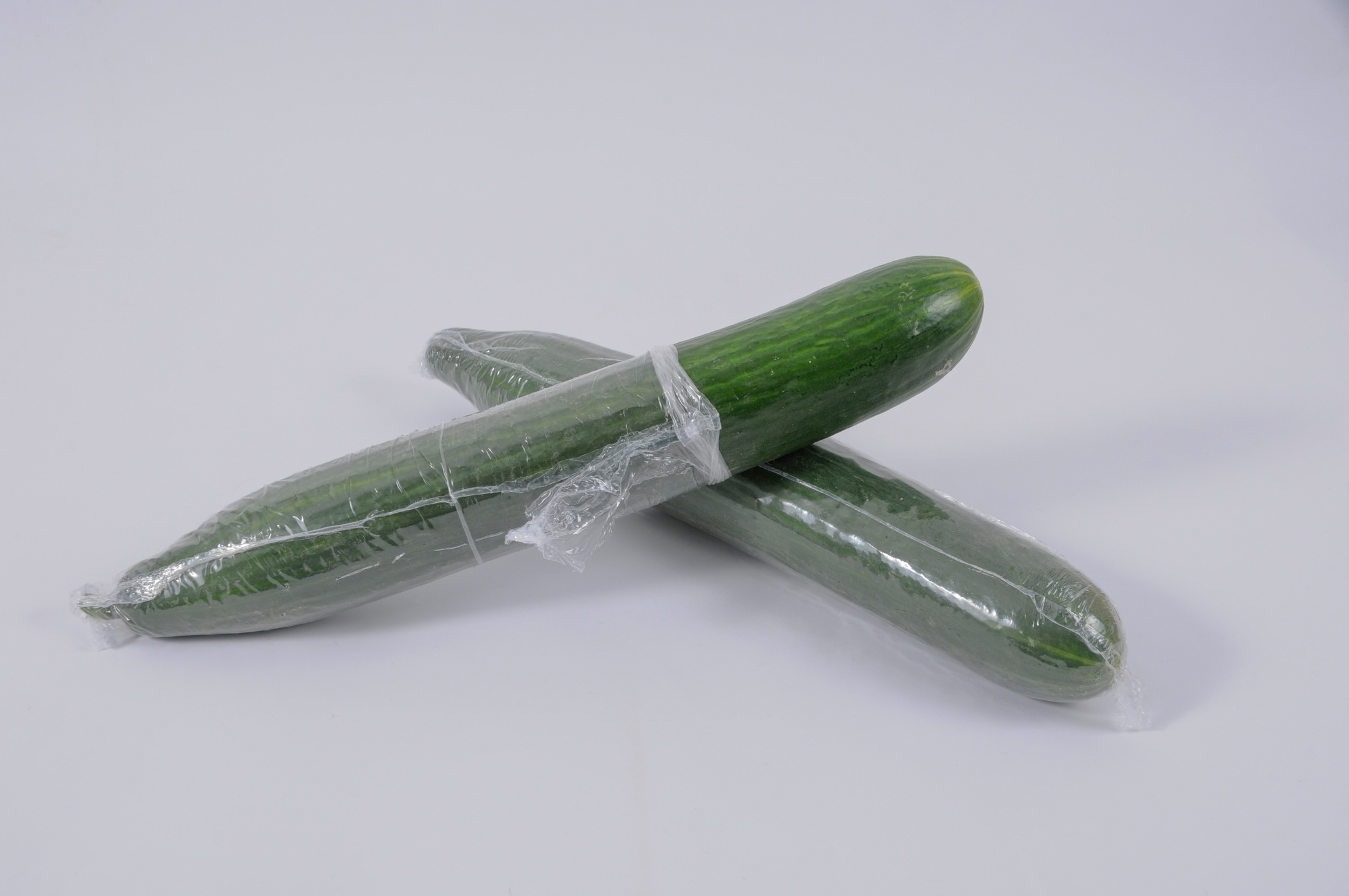 Zwei Salatgurken in Kunststofffolie verpackt. Eine Salatgurke ist zur Hälfte ausgepackt